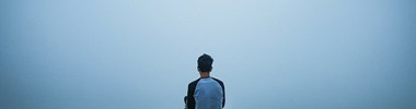 boy sitting on hill looking out into a misty landscape